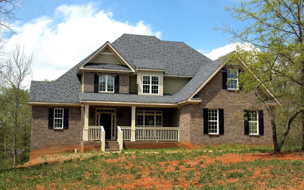 A big house with a grey roof and brown walls on a hill.