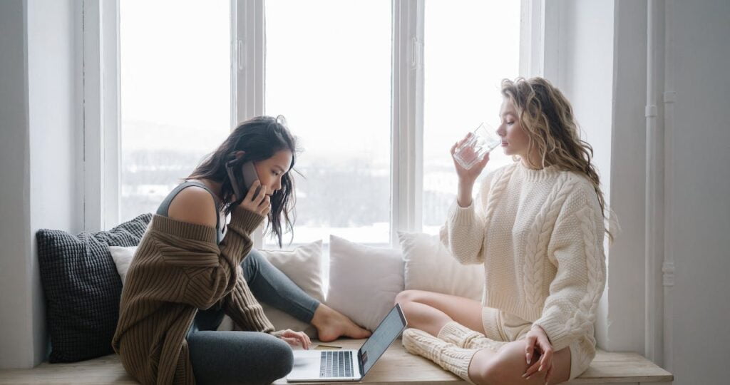 Two women sitting on a window seat and talking about window design tips.